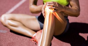 person on a running track with a sports injury holding their knee